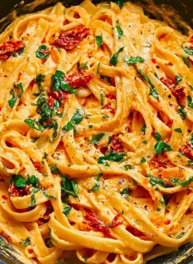 Creamy vegan sun-dried tomato pasta garnished with fresh herbs and tomatoes.