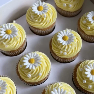Pastel yellow cupcakes decorated with daisies and pearls on a dessert table