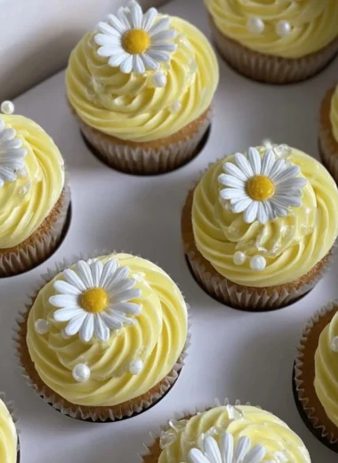 Pastel yellow cupcakes decorated with daisies and pearls on a dessert table