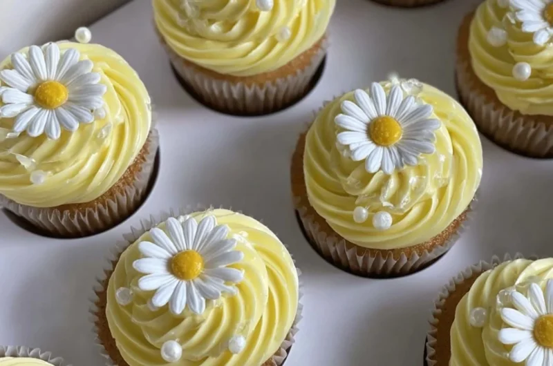 Pastel yellow cupcakes decorated with daisies and pearls on a dessert table