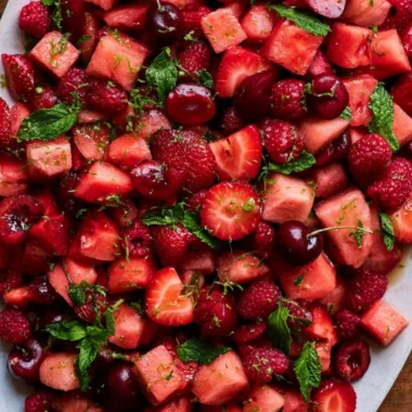 A vibrant watermelon fruit salad garnished with mint leaves and mixed fruits.