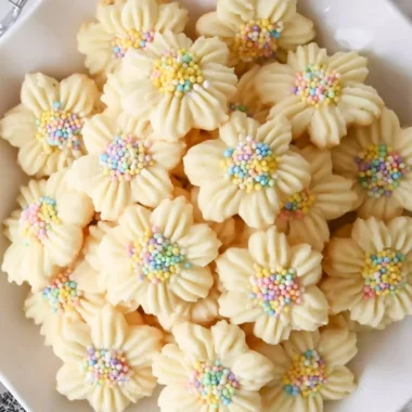 Freshly baked Lemon Spritz Cookies on a cooling rack with lemon zest garnish.