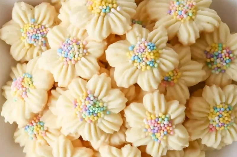 Freshly baked Lemon Spritz Cookies on a cooling rack with lemon zest garnish.